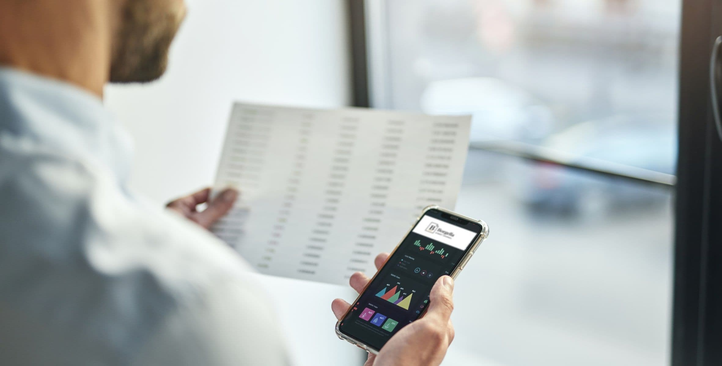 A hand holding a phone open on the Borgella app beside a printed report